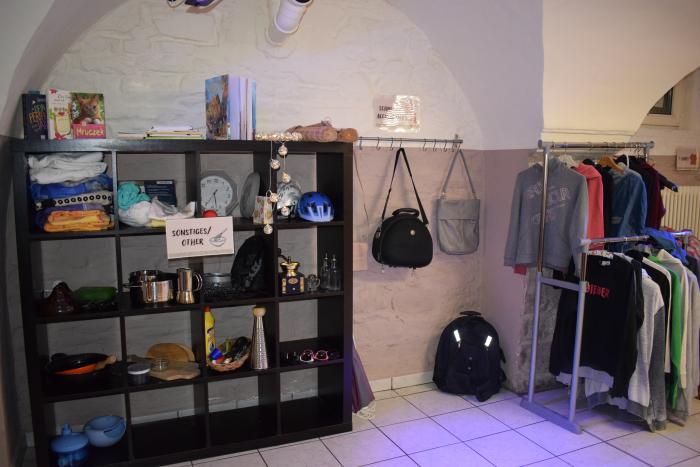 Kleidungsstücke und Accessoires hängen in Regalen und an Kleiderstangen. 